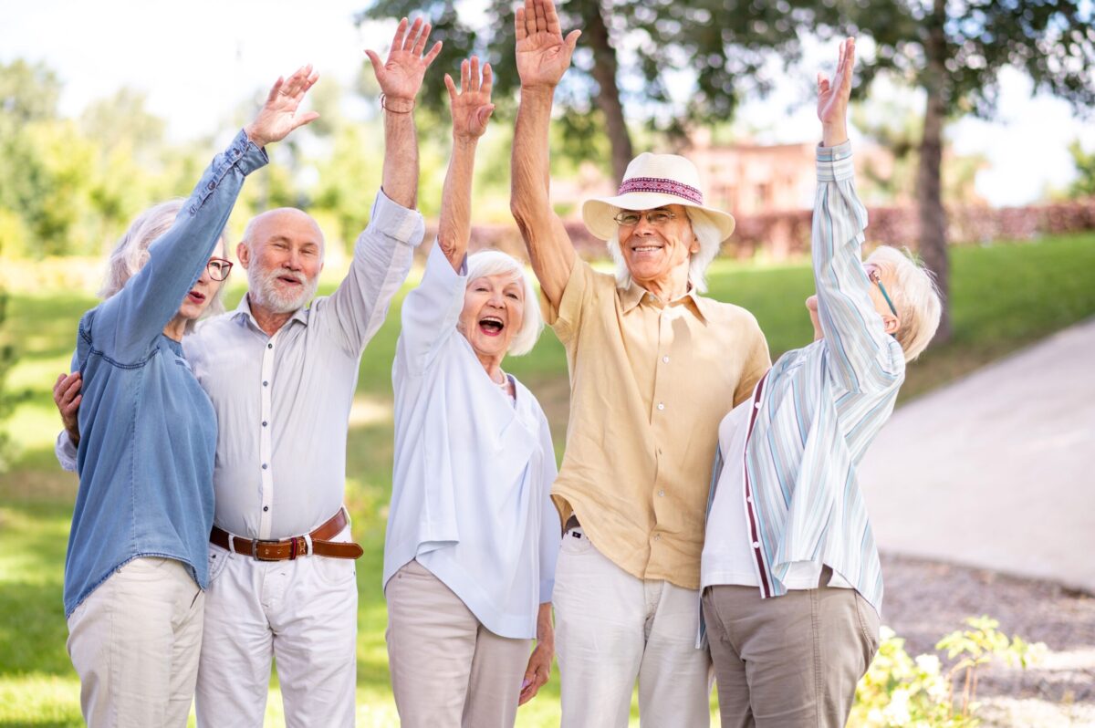 Group of older adults raising their hands joyfully outdoors in an independent living Chattanooga community
