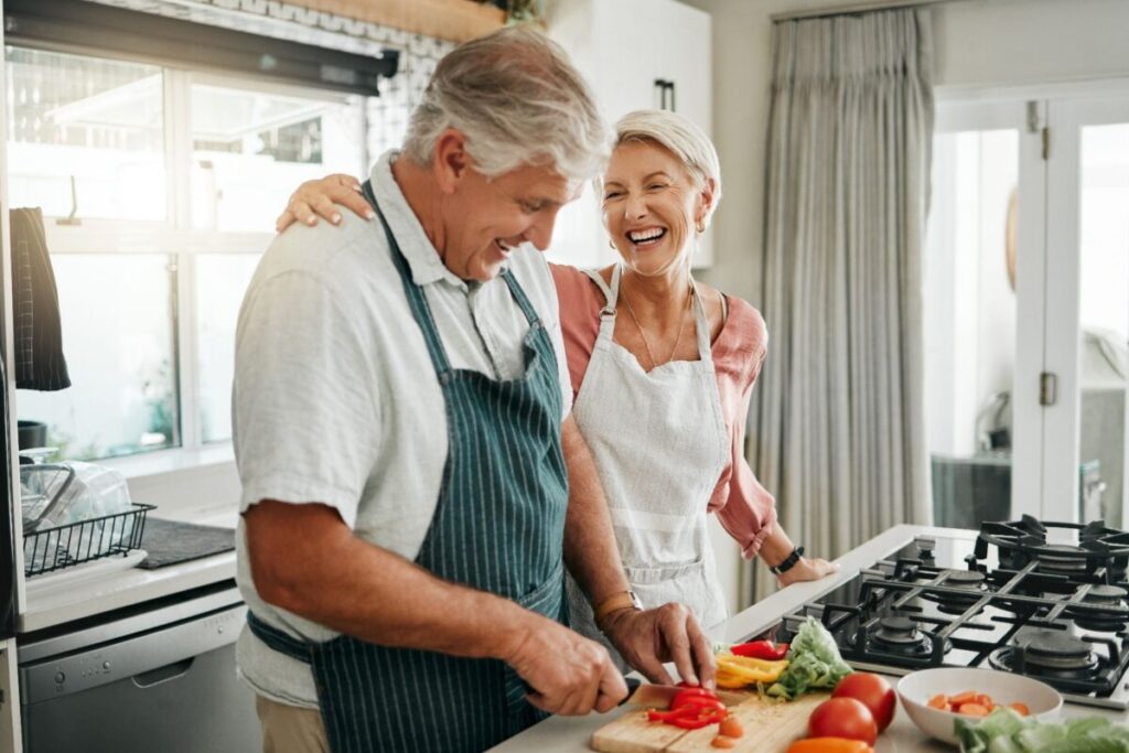 Older couple cooking together in a bright kitchen, representing balancing independence in senior living.