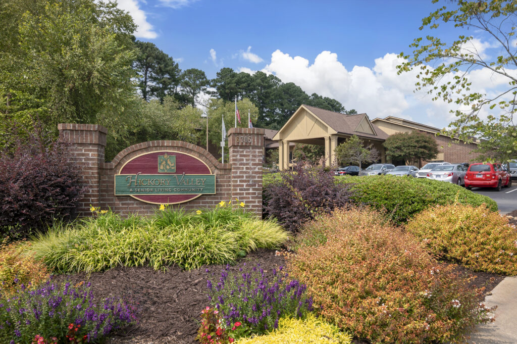 The entrance sign for Hickory Valley, a senior living community in Chattanooga, surrounded by colorful landscaping and lush greenery on a sunny day.