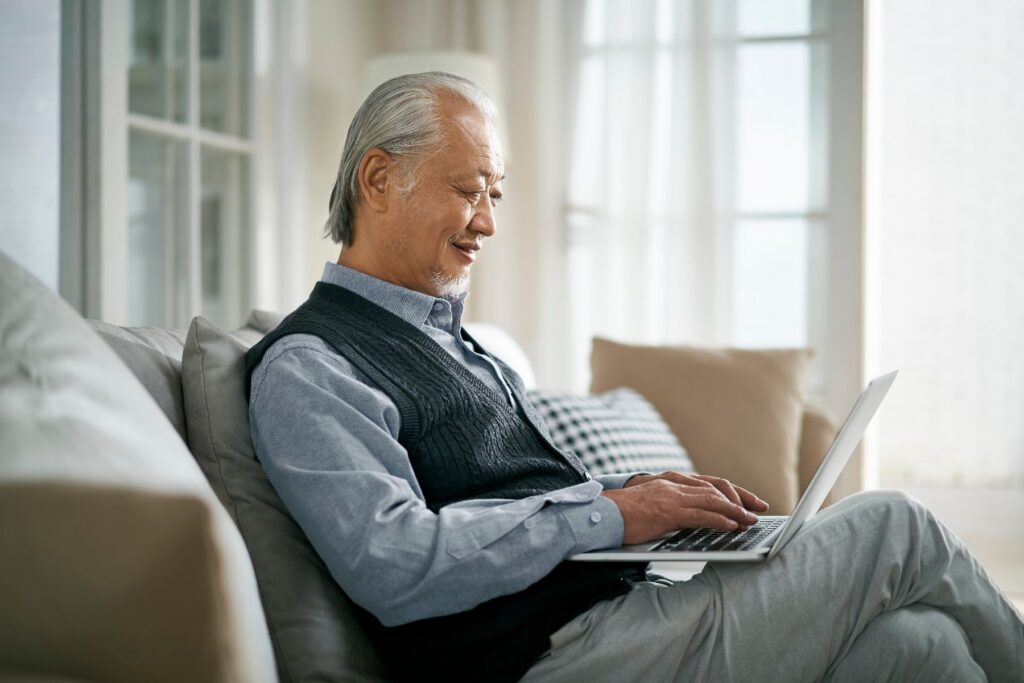An older man relaxes on his sofa with a laptop, enjoying a quiet afternoon that reflects the comfort and freedom of independent living in Chattanooga, TN.